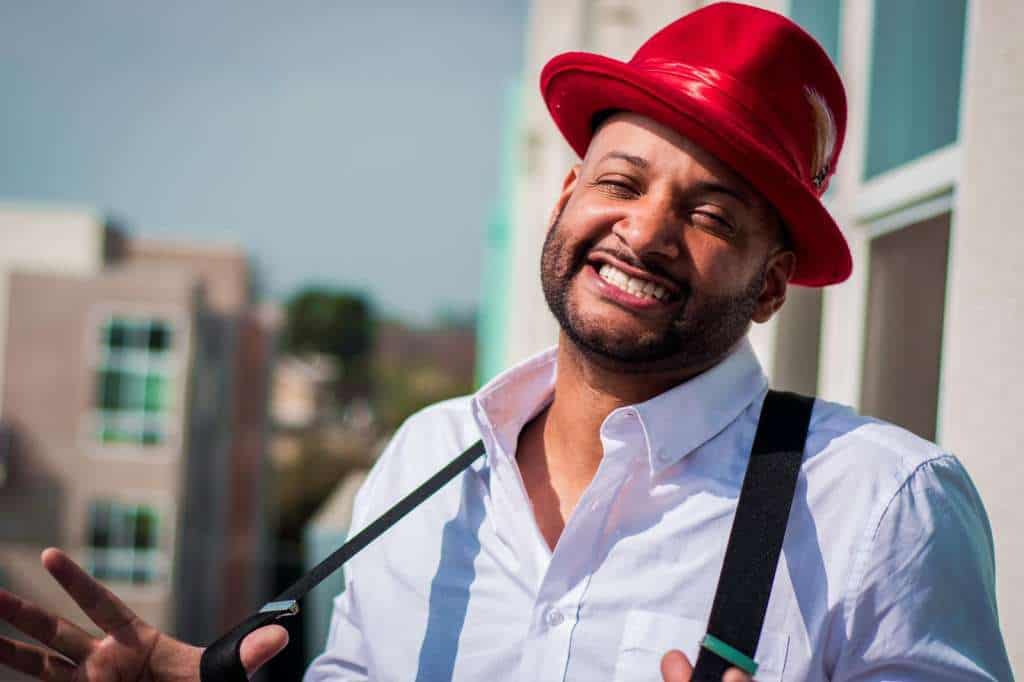 Stylish man wearing a red hat and white shirt smiling outdoors, showcasing fashion and personality.