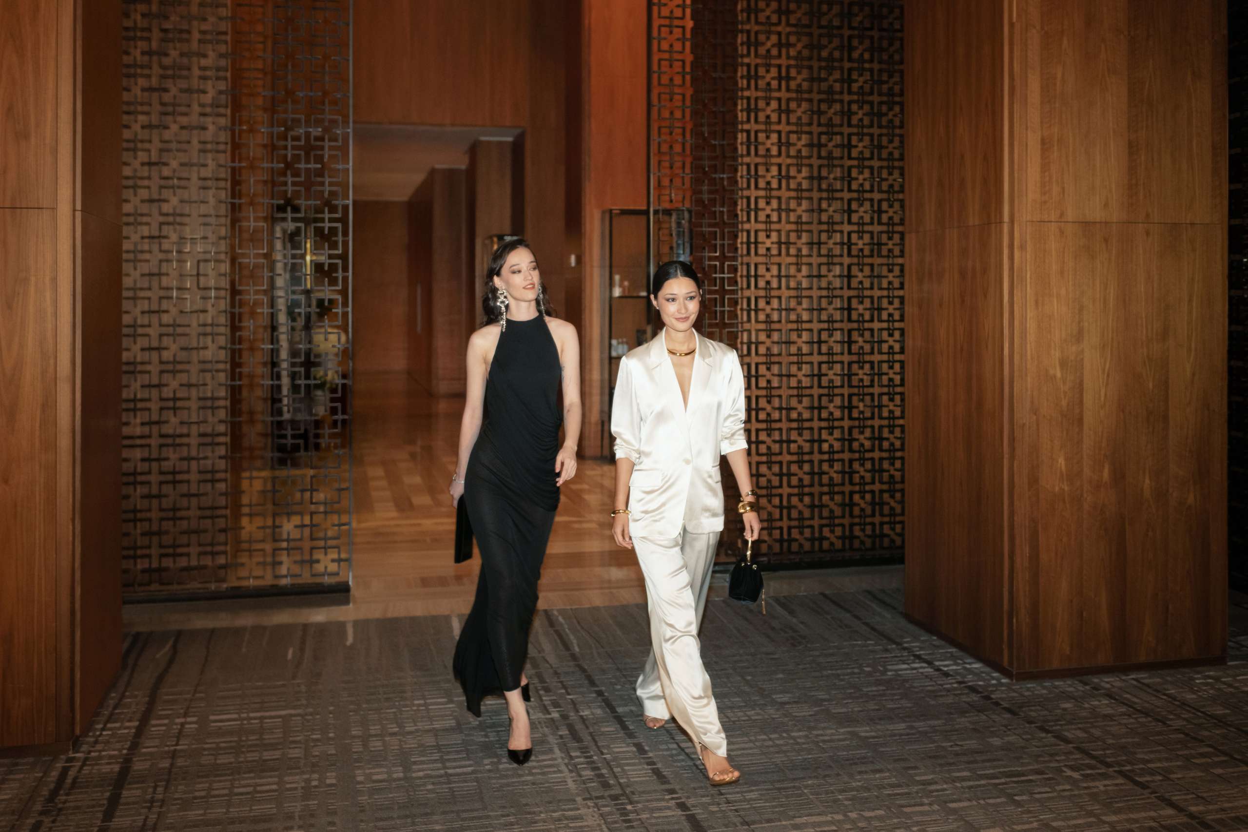 Two elegantly dressed guests walking through Four Seasons Hotel Toronto with evening handbags