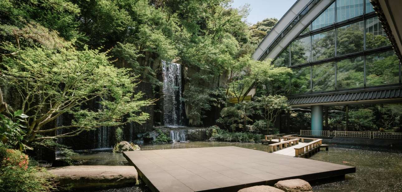 A garden pond, stepping stones and waterfall beside the modern glass exterior of Hotel Gajoen Tokyo.